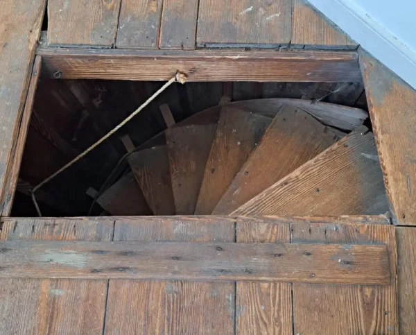 A wooden spiral staircase in the middle of an attic.