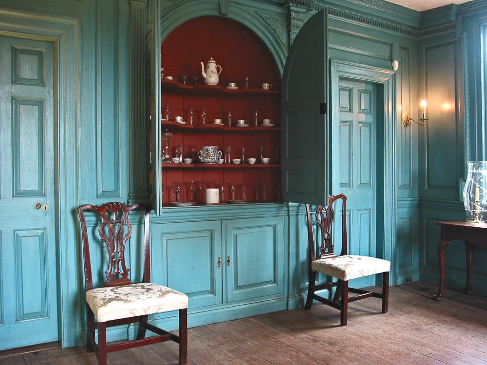 A blue cabinet with two chairs in front of it.