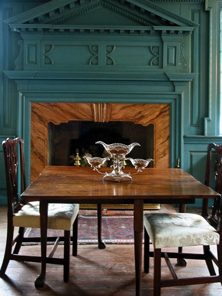 A table with chairs and a fireplace in the background.