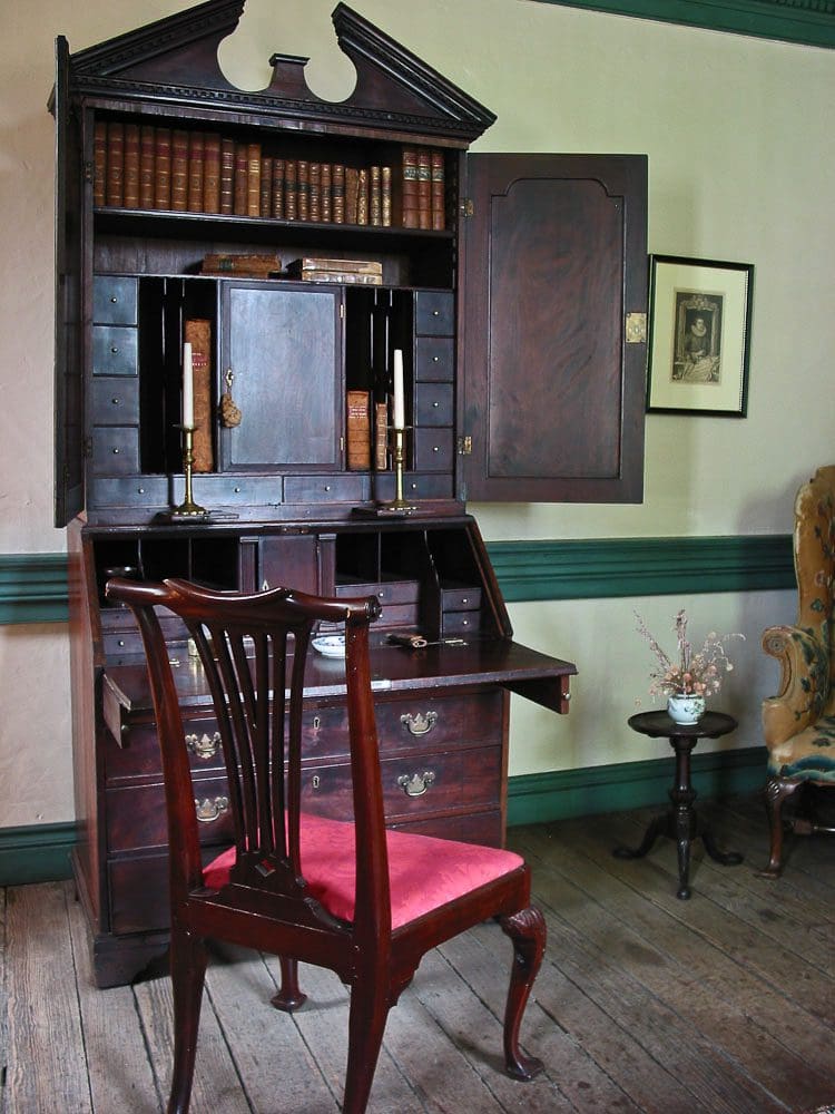 A chair and desk in front of an antique writing desk.