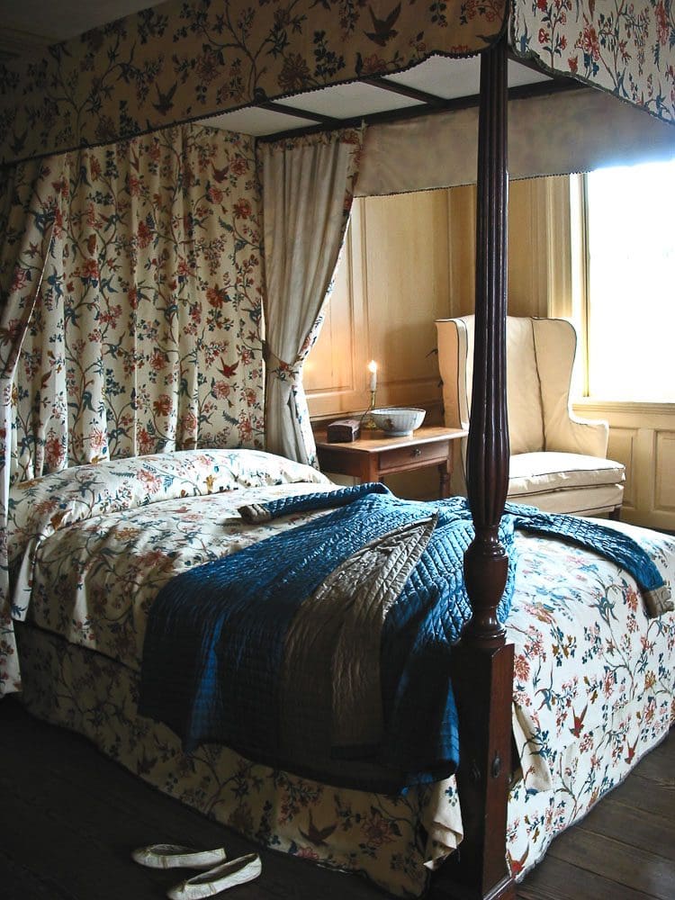 A bed with floral curtains and blue blanket.