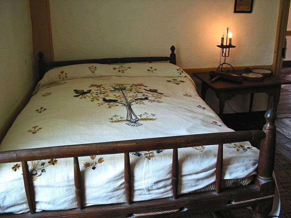 A bed with an embroidered bedspread and a candle.